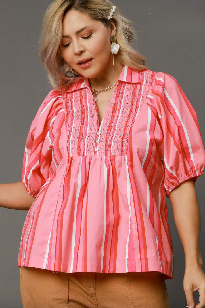 A woman wearing a coral pink stripe smocked top with short puffed sleeves and a round neckline.