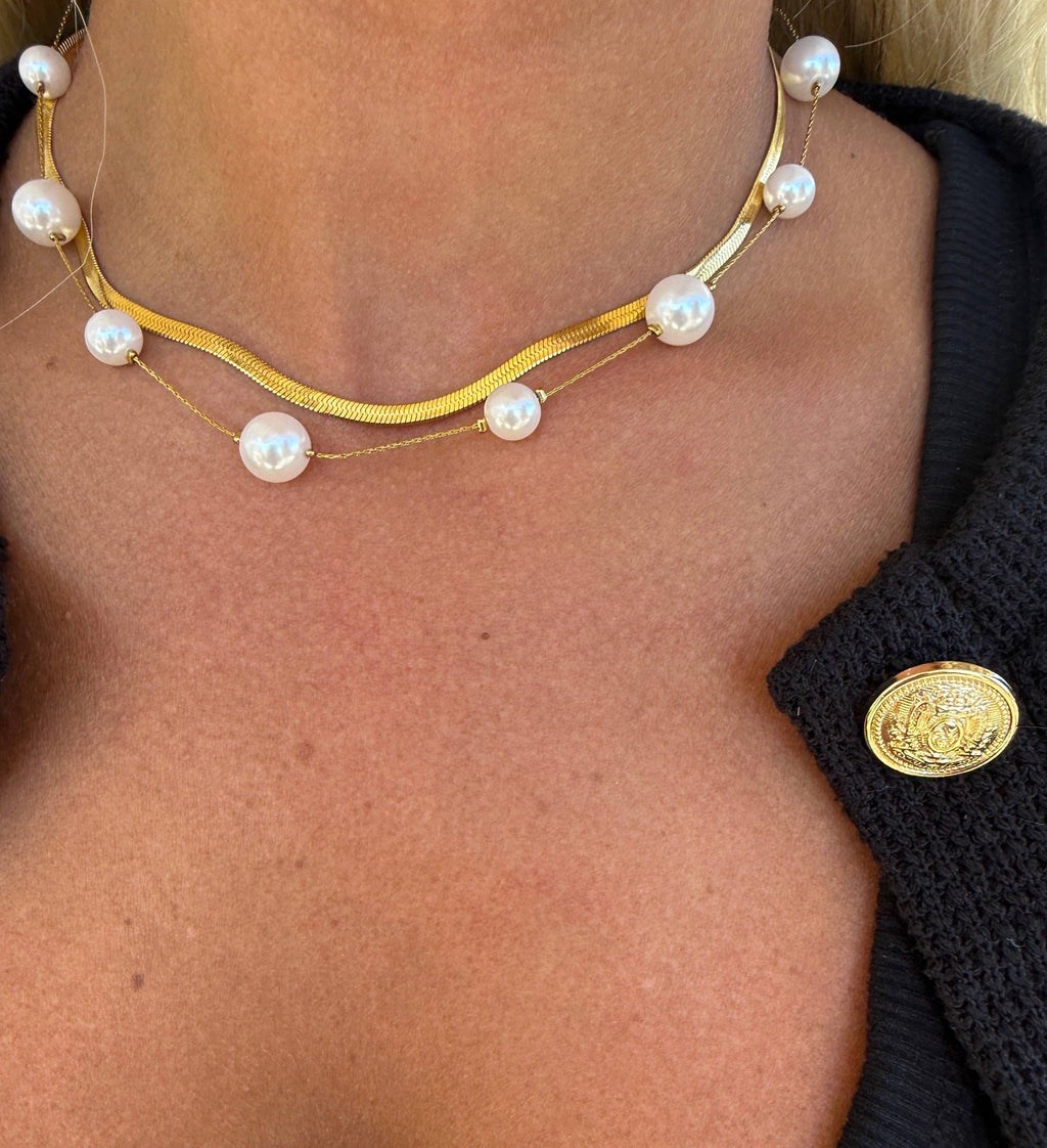 Gold necklace with pearls worn by a person, close-up view.