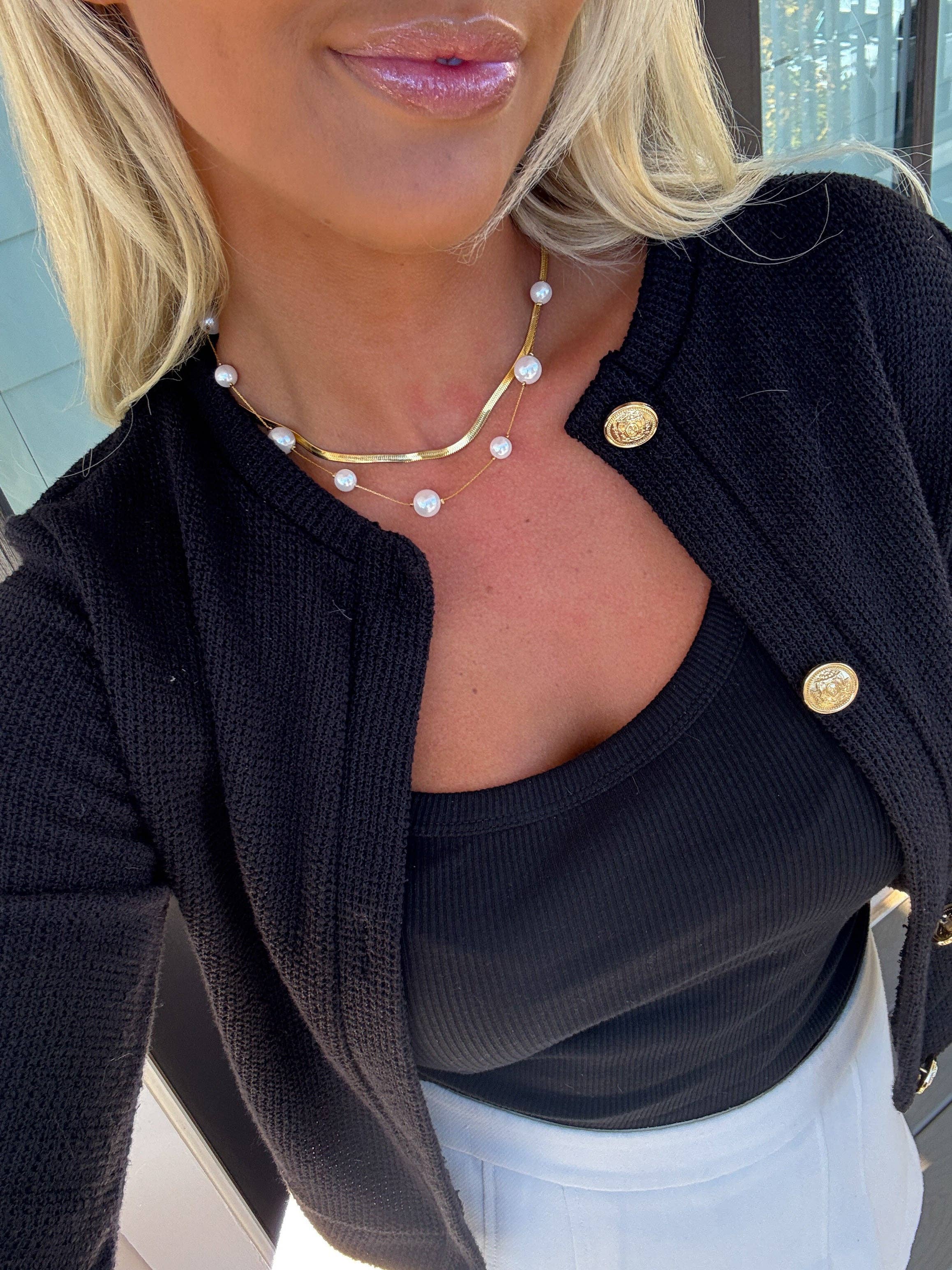 Person wearing a black cardigan with gold buttons, pearl necklace, and pink lipstick.