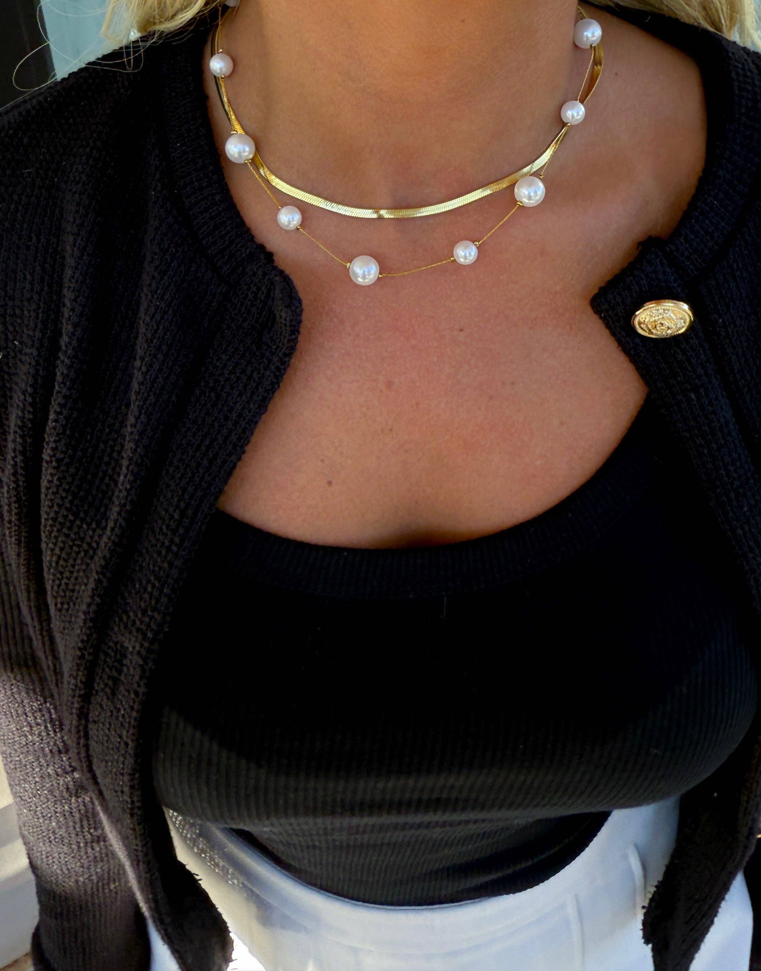 Close-up of a person wearing a pearl necklace and black cardigan.