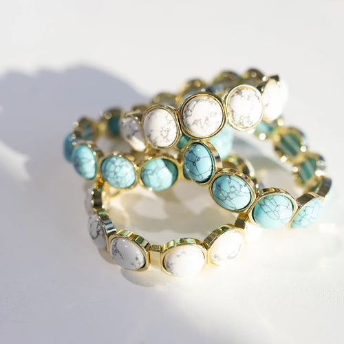 Set of turquoise and gold beaded bracelets on a white surface