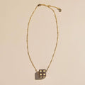A gold beaded chain necklace with a dark metallic dice pendant showing four white dots, displayed on a warm beige background.
