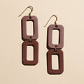 A pair of rectangular drop earrings with a matte dark reddish-brown finish and gold-tone fishhook wires, displayed on a light beige background.