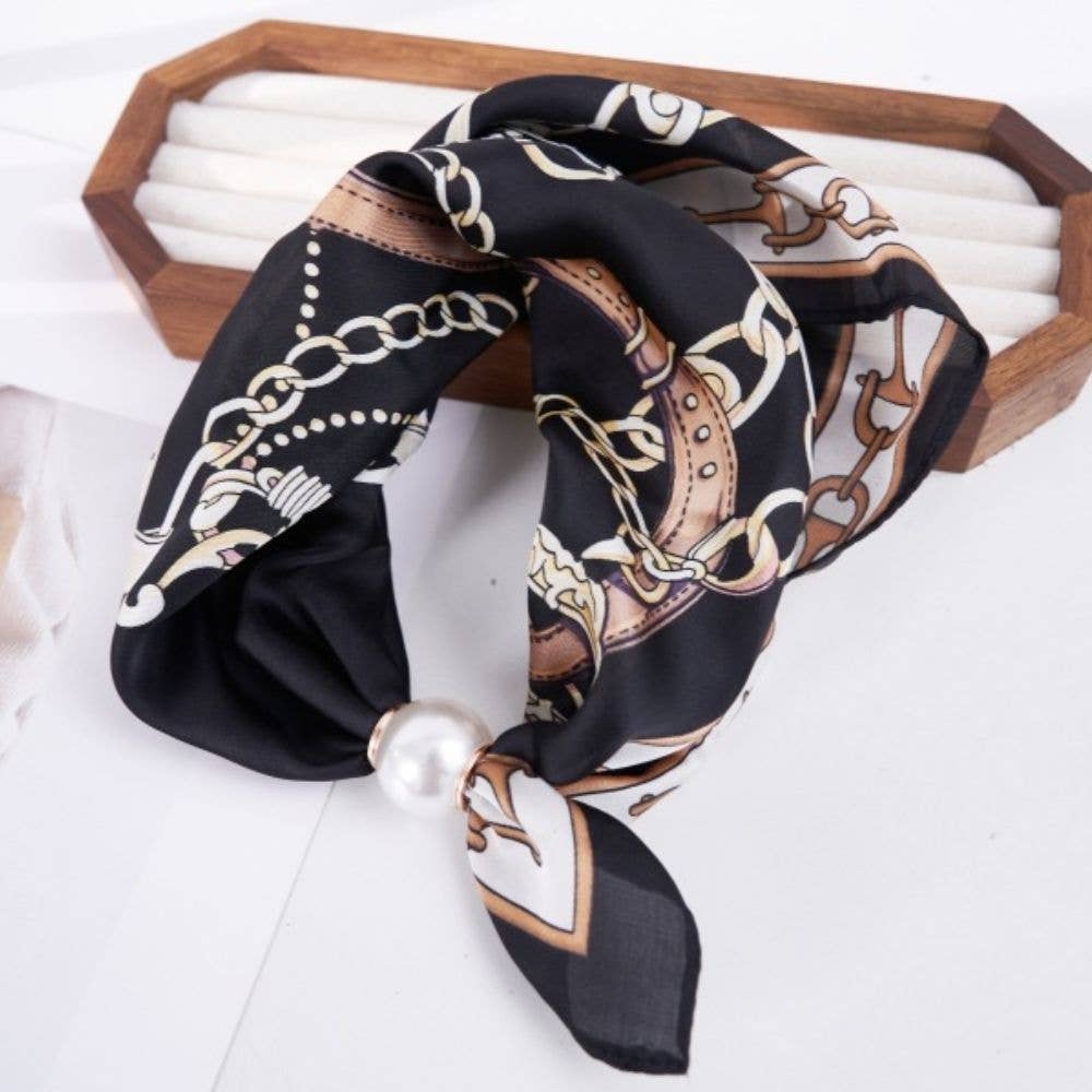A black silk scarf with a brown and beige chain-link pattern and a white pearl accent, draped over a wooden jewelry display box on a white surface.