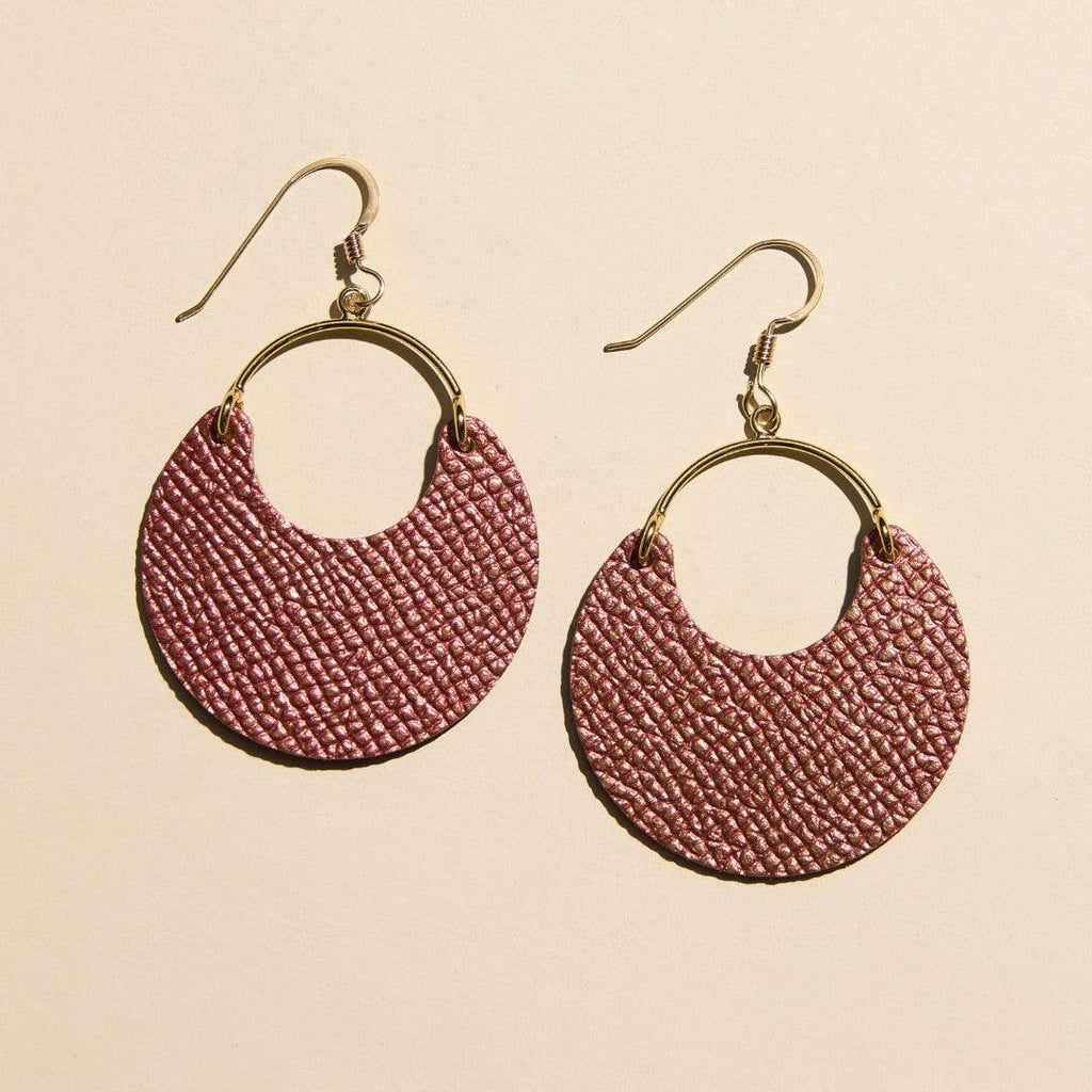 A pair of handmade dangle earrings featuring textured, woven dusty rose semicircular discs attached to gold-tone metal hoops and fishhook ear wires, displayed on a solid light beige background.