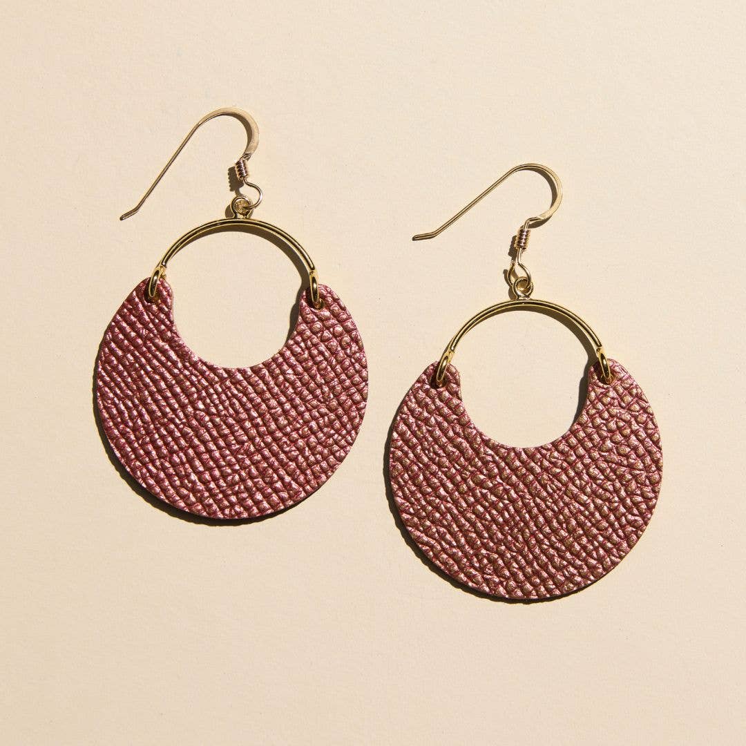 A pair of handmade dangle earrings featuring textured, woven dusty rose semicircular discs attached to gold-tone metal hoops and fishhook ear wires, displayed on a solid light beige background.