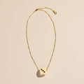 A delicate gold chain necklace featuring a cream-colored dice pendant with black pips, displayed on a warm beige background.