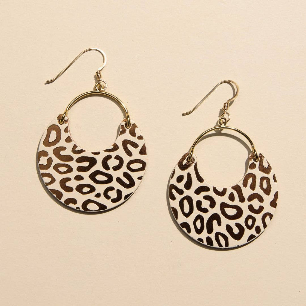 A pair of gold-tone hoop earrings with crescent-shaped dangles featuring a brown and beige leopard print pattern, shown on a warm beige background.