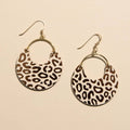 A pair of gold-tone hoop earrings with crescent-shaped dangles featuring a brown and beige leopard print pattern, shown on a warm beige background.