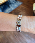 A close-up of a person's wrist wearing a silver cuff bracelet adorned with multiple teardrop-shaped gemstones in shades of brown, amber, and smoky gray.