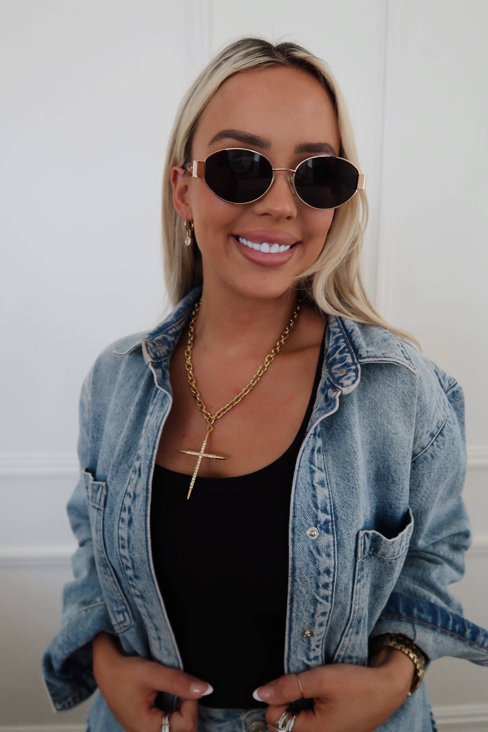 Woman wearing sunglasses, denim jacket, and black top against a white background