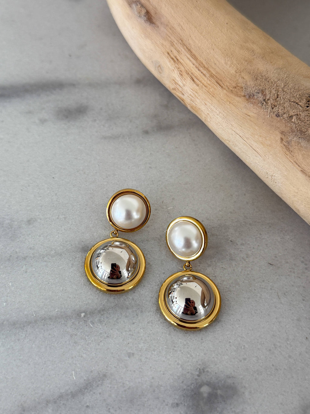 Pair of earrings with gold and pearl design on a gray surface