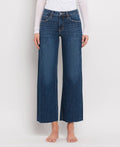 Women's mid-rise dark wash wide leg jeans featuring tummy control panels, comfort stretch denim, cropped length, and a raw hem.