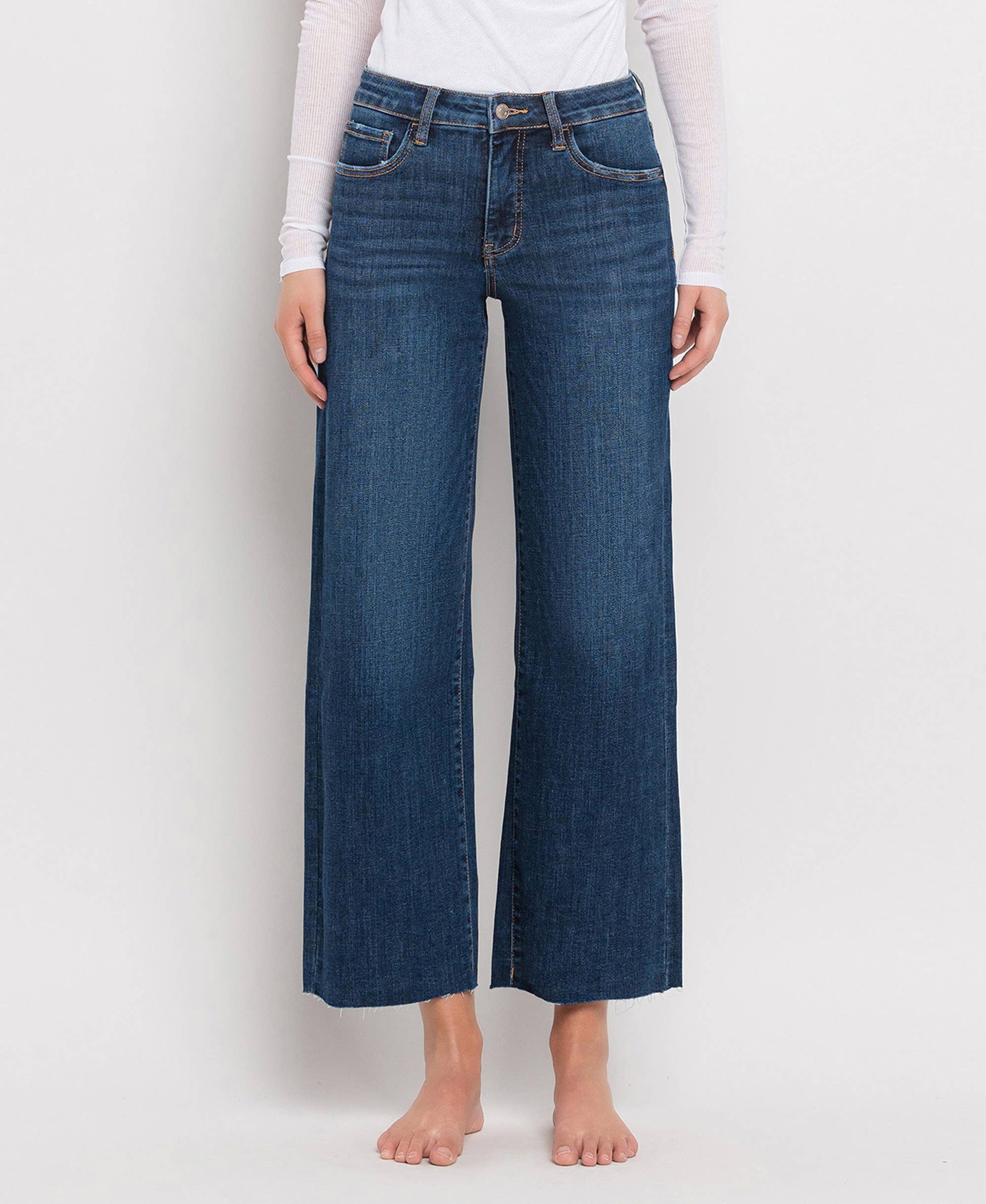 Women's mid-rise dark wash wide leg jeans featuring tummy control panels, comfort stretch denim, cropped length, and a raw hem.