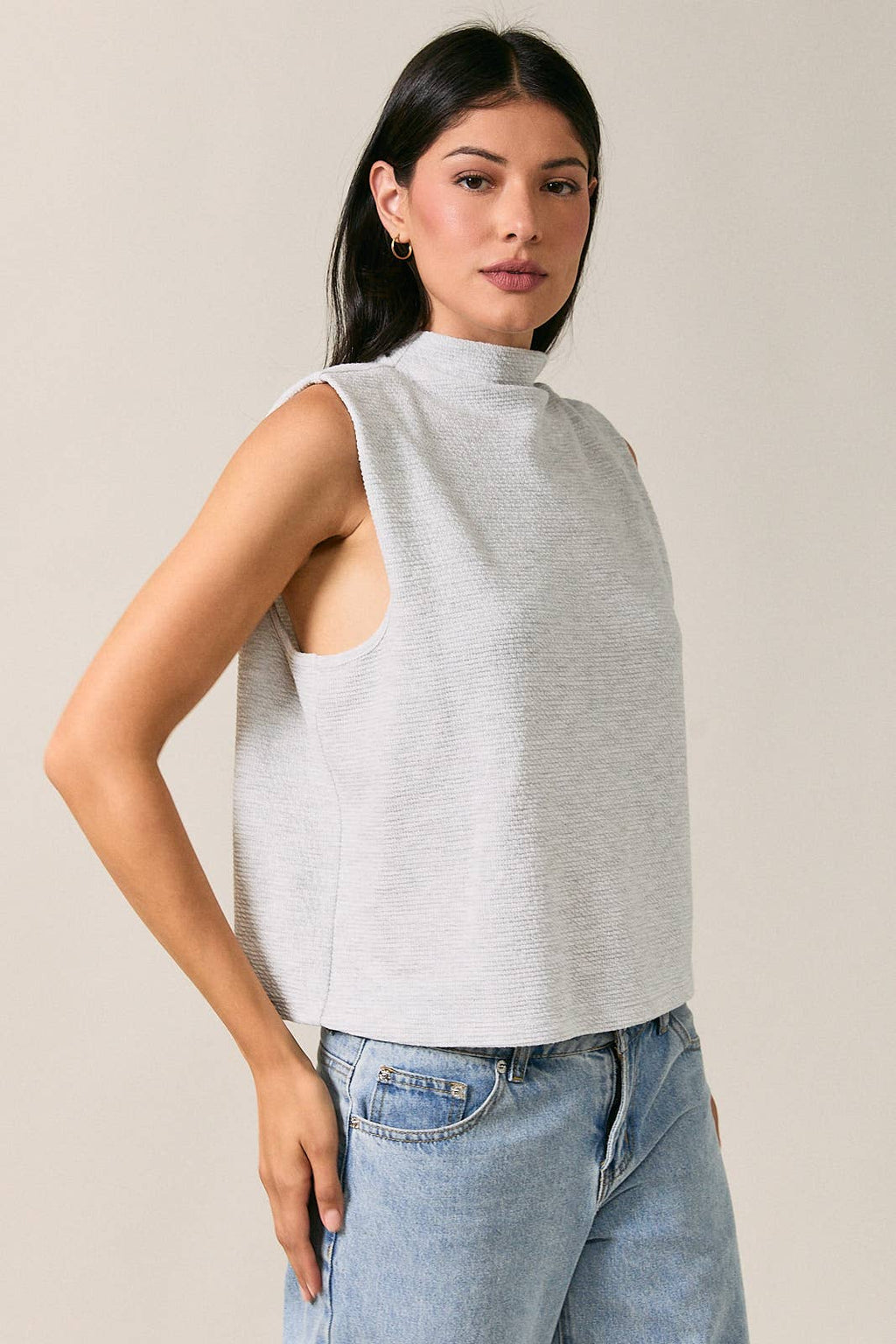 Side view of a women's light heather gray sleeveless mock neck top with structured folded shoulders.