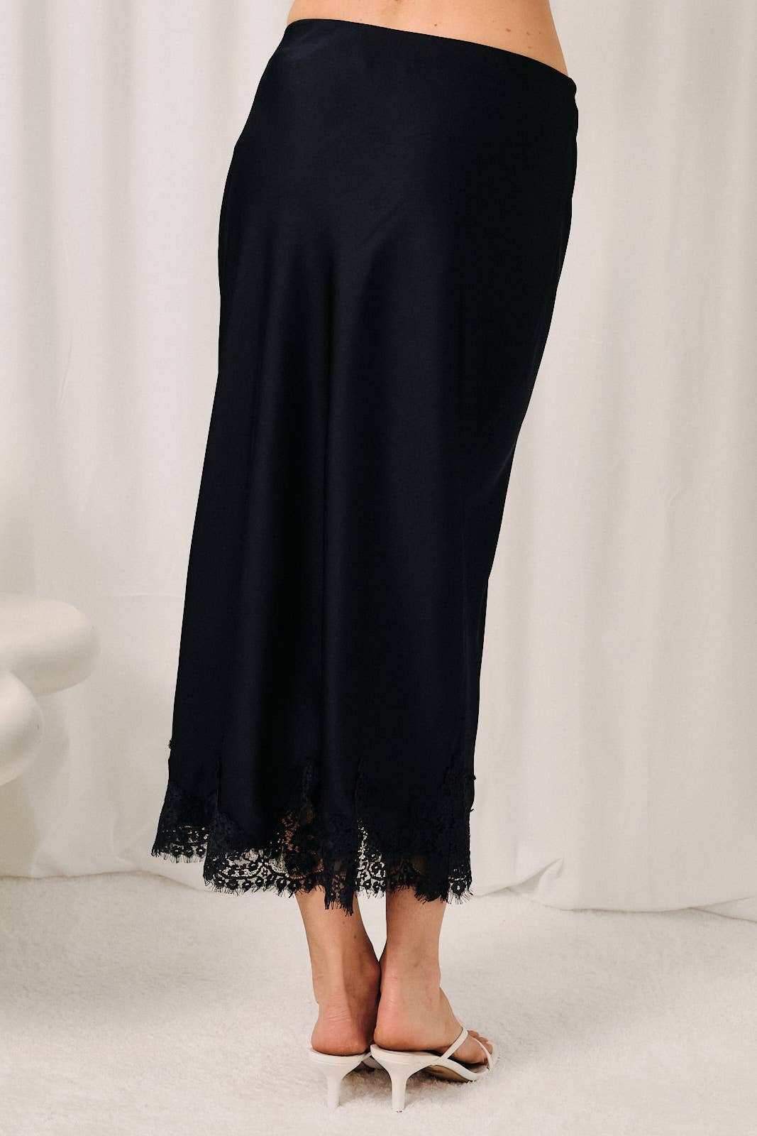 Back view of navy satin midi skirt with lace applique detailing and a bias cut silhouette.