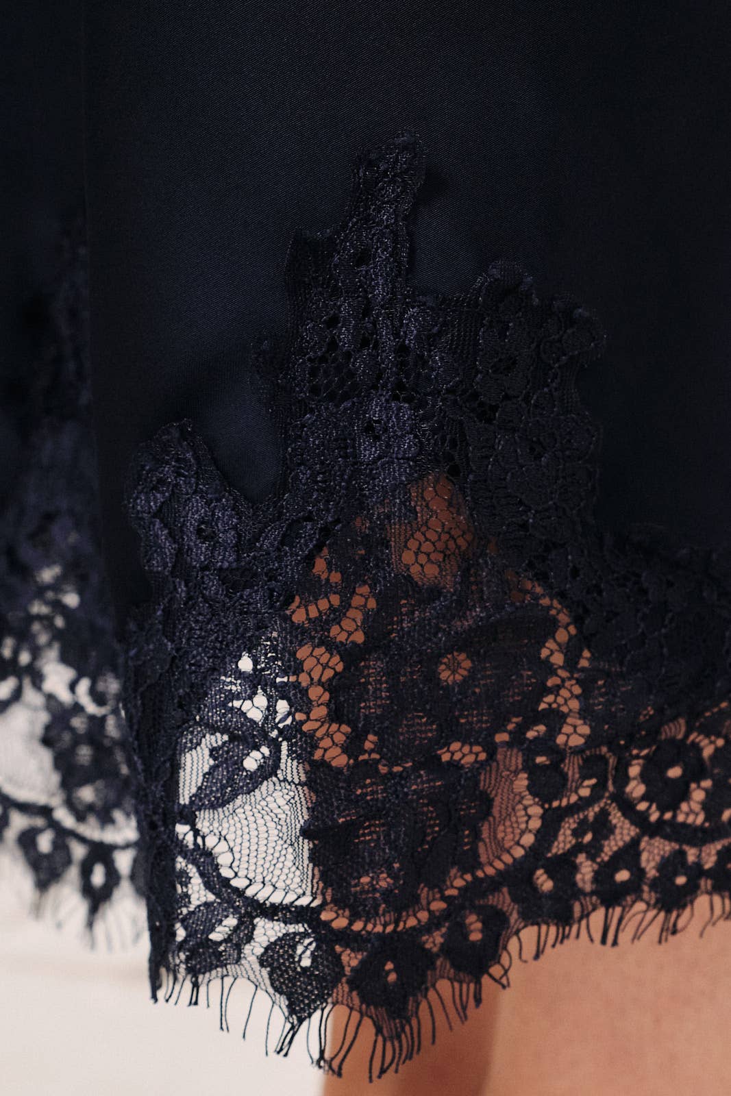 Close-up of delicate lace applique detailing on a navy satin midi skirt.