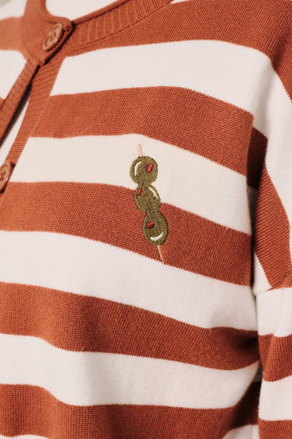Close-up of olive embroidered design on the front of a rust and white striped cardigan.