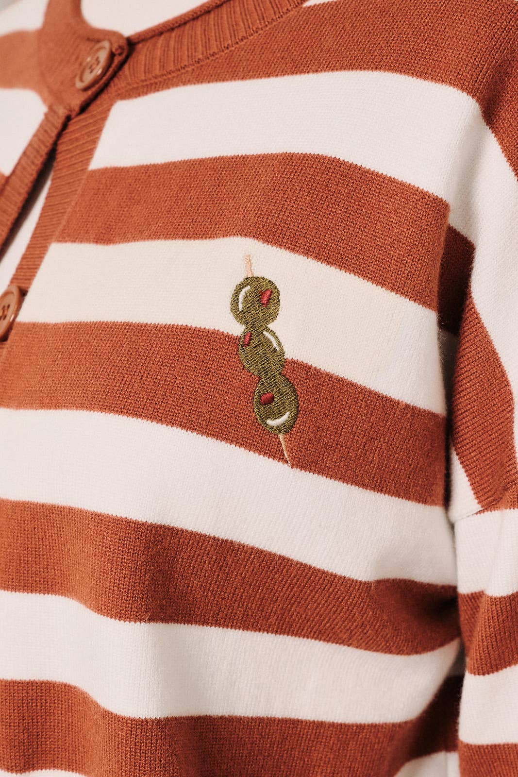 Close-up of olive embroidered design on the front of a rust and white striped cardigan.