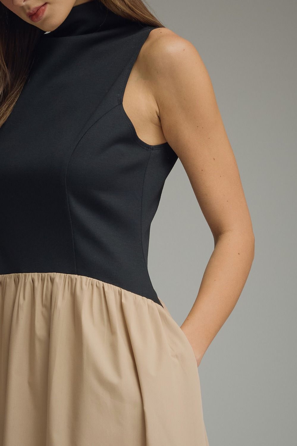 Side view of a black sleeveless mock neck midi dress with a flowing khaki skirt.