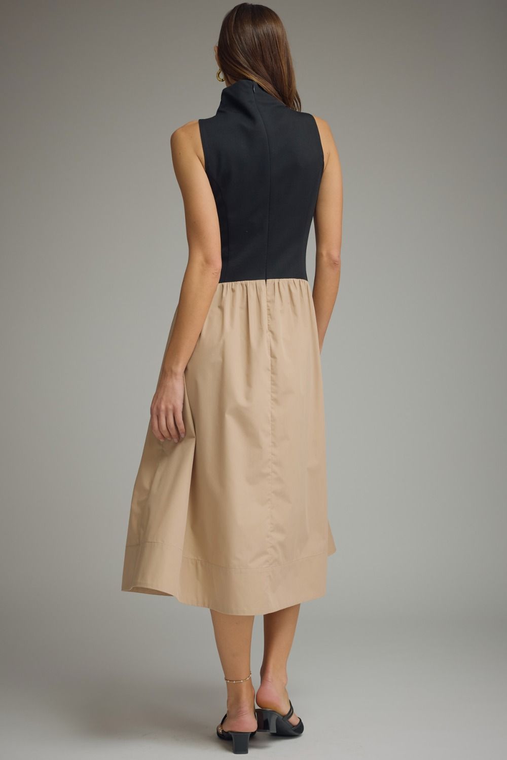 Back view of a mixed media midi dress featuring a black knit bodice and khaki skirt with zipper closure.