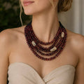 A close-up of a woman wearing a multi-strand beaded necklace with deep burgundy beads and three light beige stone accents, paired with a beige strapless top.