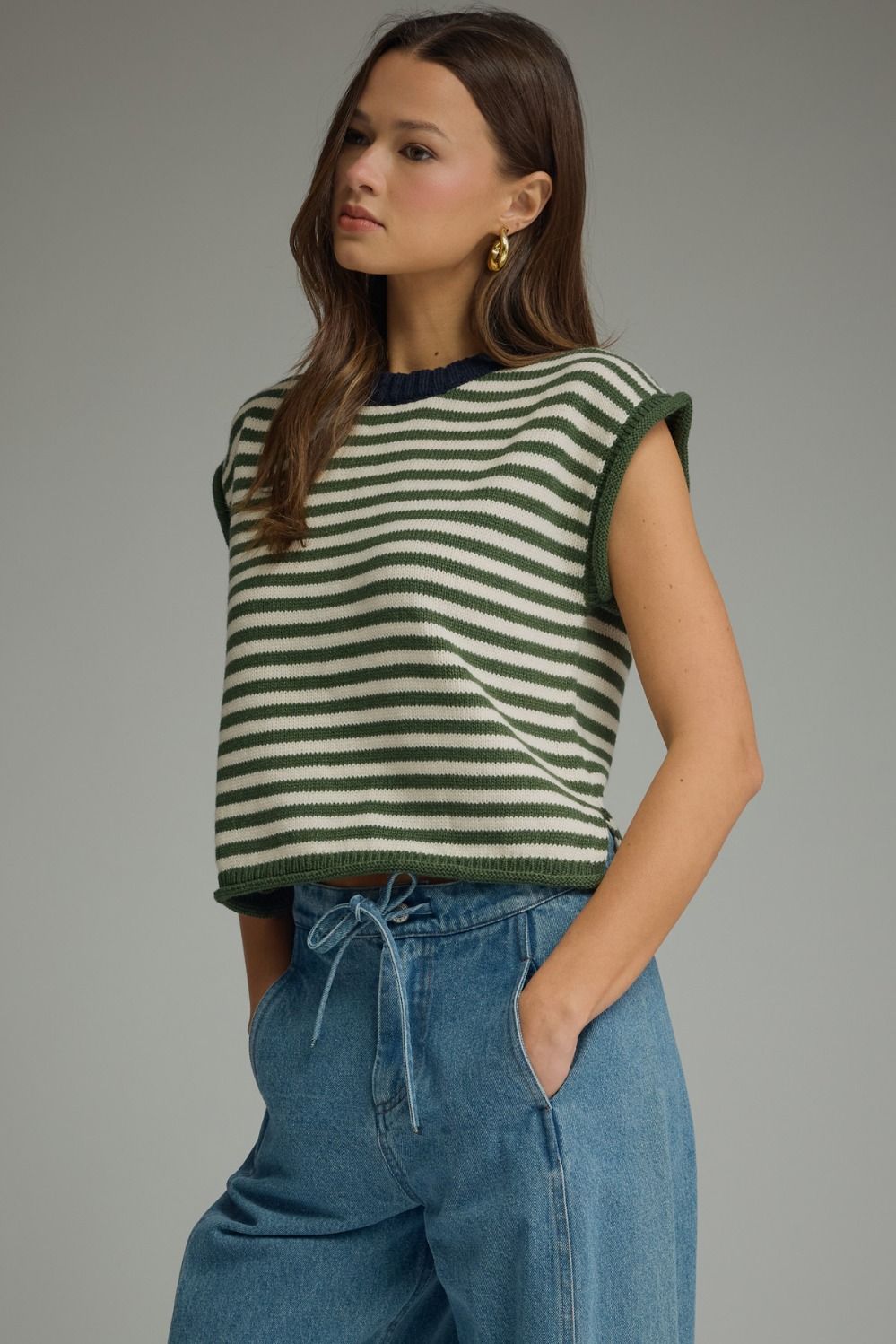 Woman wearing a green and white striped sleeveless top with blue jeans on a gray background