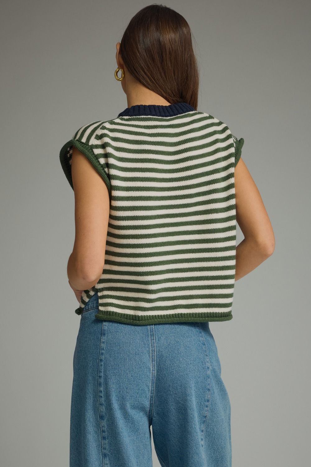 Person wearing a green and white striped sleeveless top with blue jeans on a gray background