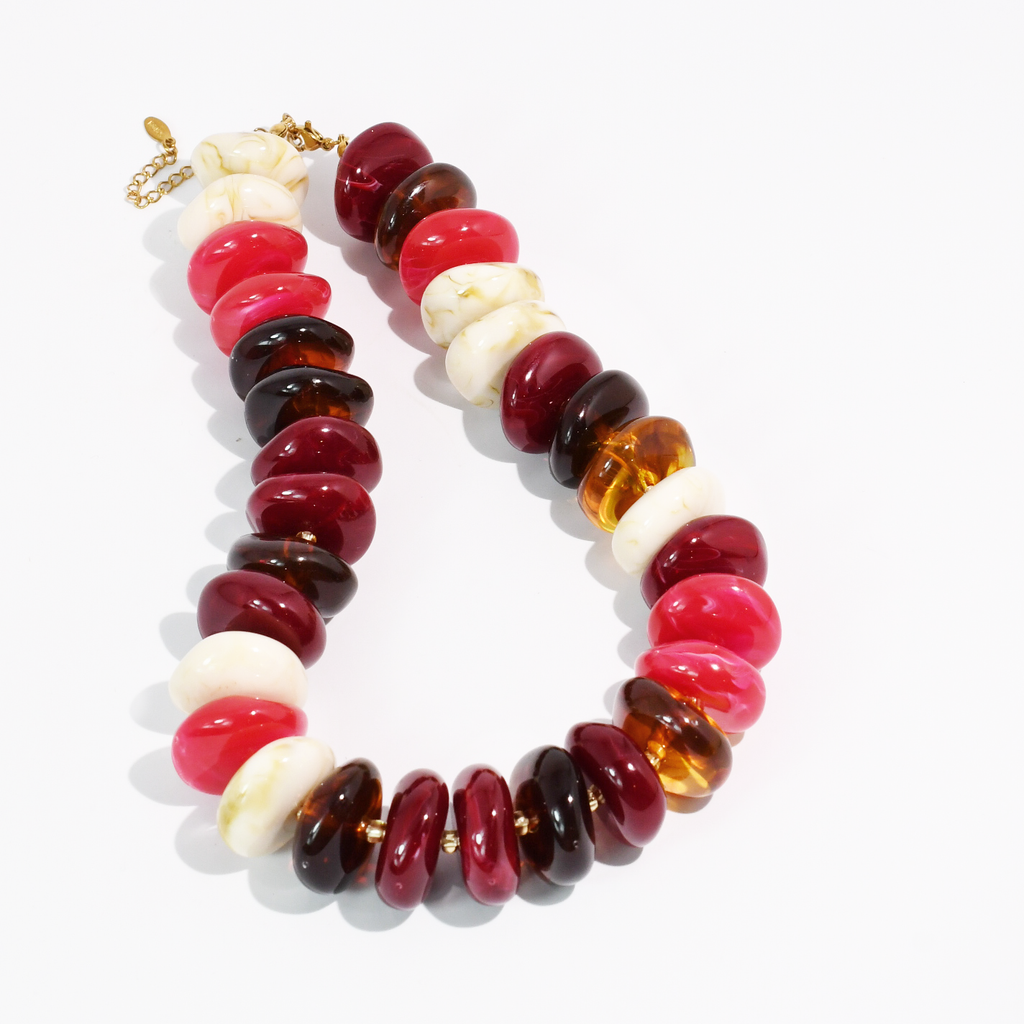 A chunky beaded necklace featuring alternating glossy dark red, translucent amber, deep brown, and matte white disc-shaped beads, accented with small gold spacer rings and a gold clasp, shown on a clean white background.