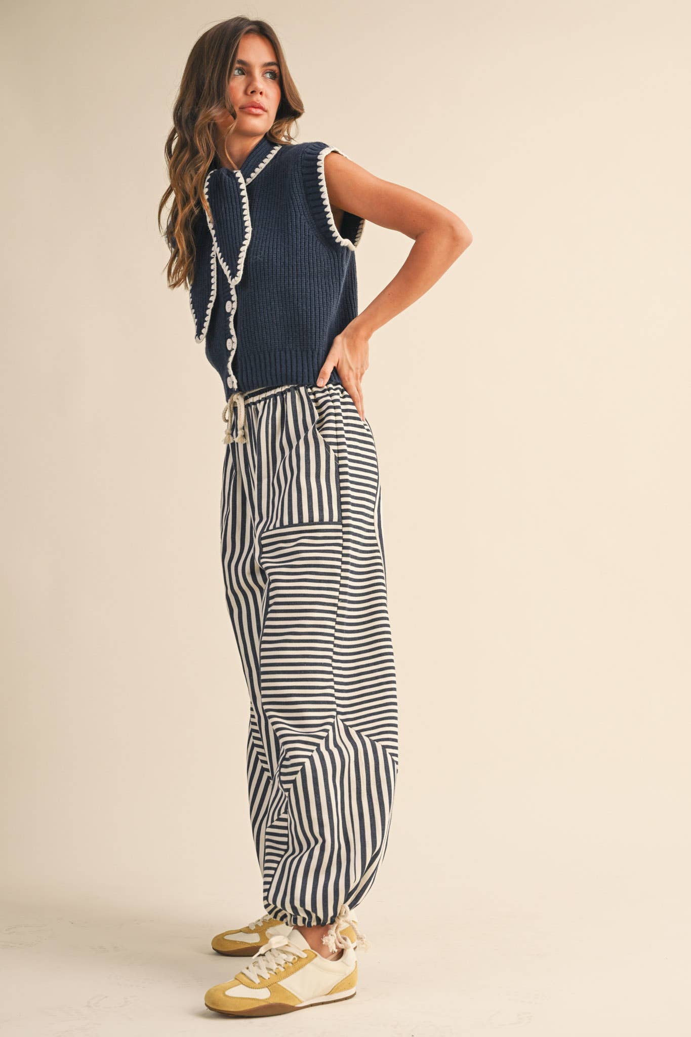 Woman wearing a blue sleeveless top and striped pants on a beige background