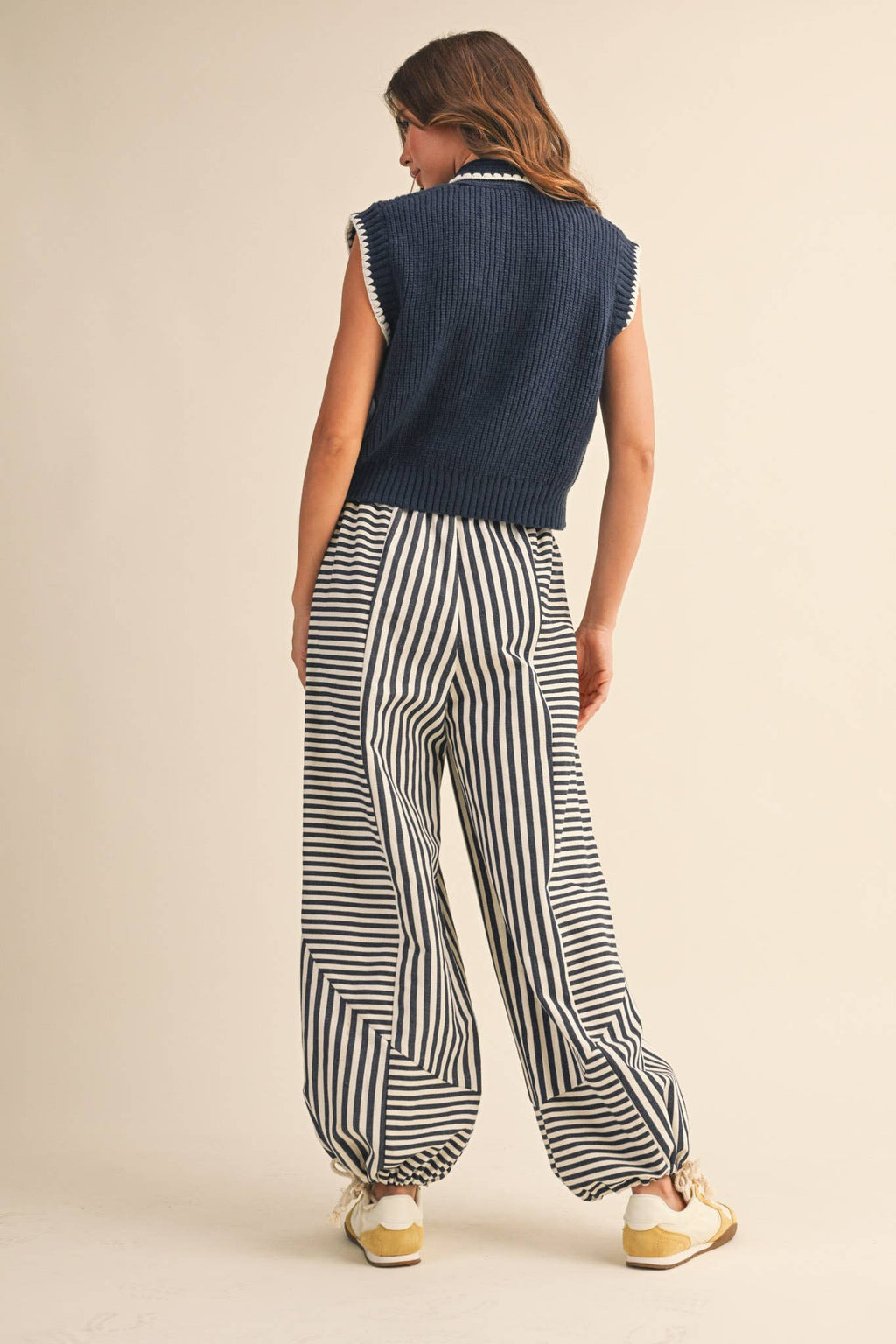 Woman wearing a navy sleeveless top and black and white striped pants on a beige background