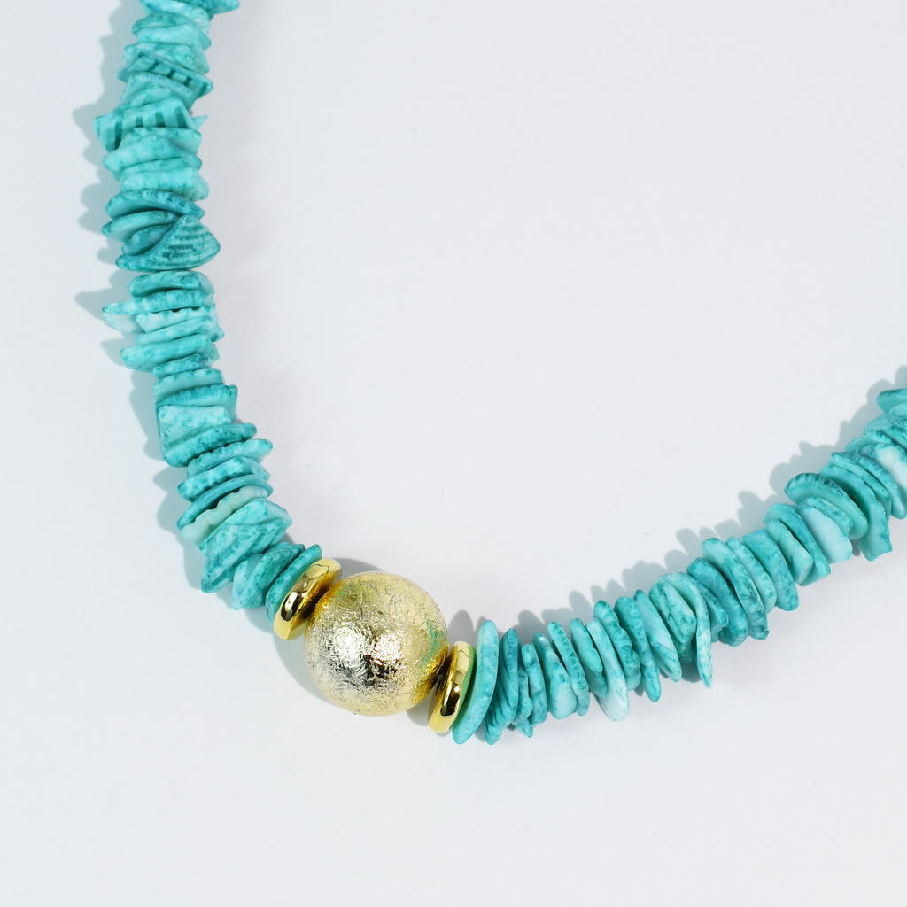 Turquoise beaded necklace with a gold accent on a light gray background