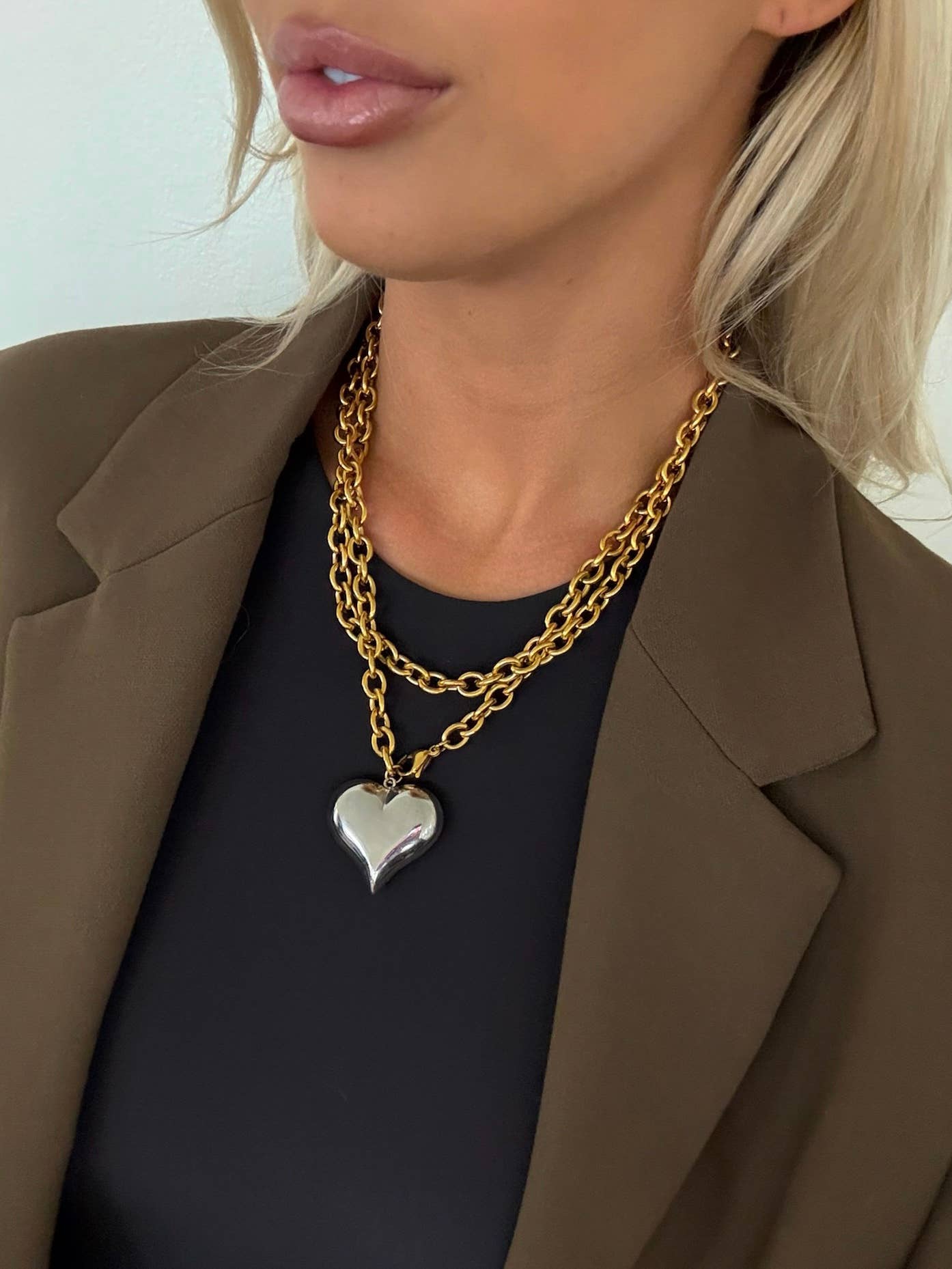 Person wearing a gold chain necklace with a heart pendant, close-up shot.