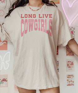 Person wearing a beige t-shirt with 'LONG LIVE COWGIRLS' text in pink, standing against a colorful wall.