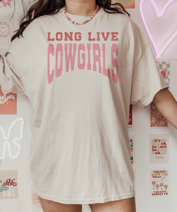 Person wearing a beige t-shirt with 'LONG LIVE COWGIRLS' text in pink, standing against a colorful wall.